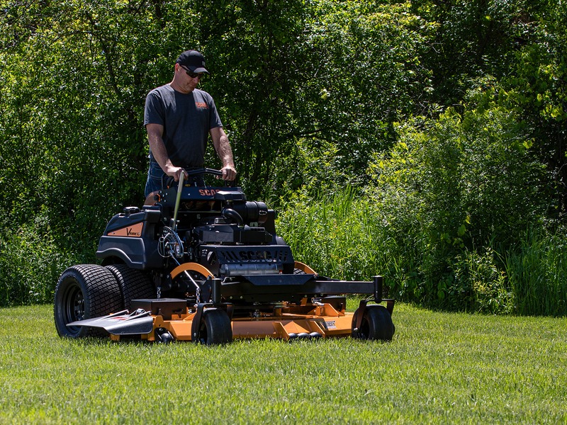 Operator riding a commercial stand-on mower across a green lawn